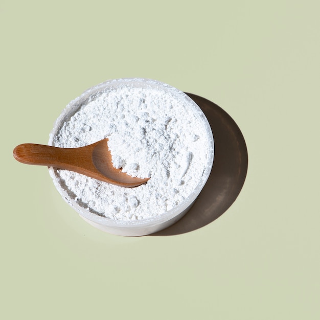 Bowl of white powder with a wooden spoon on a light green background.