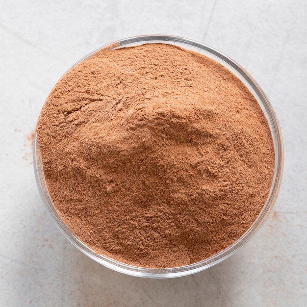 Bowl of brown powdered spice on a light surface.