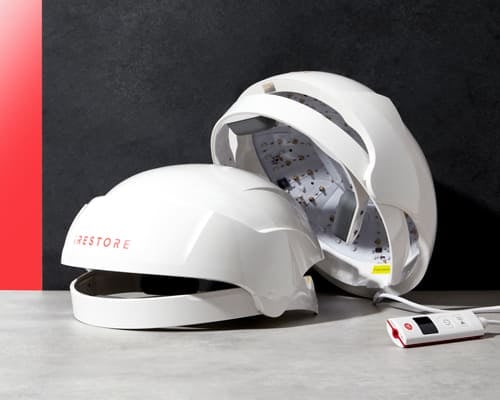 Two white iRestore hair growth helmets with LEDs and a control device on a grey table.