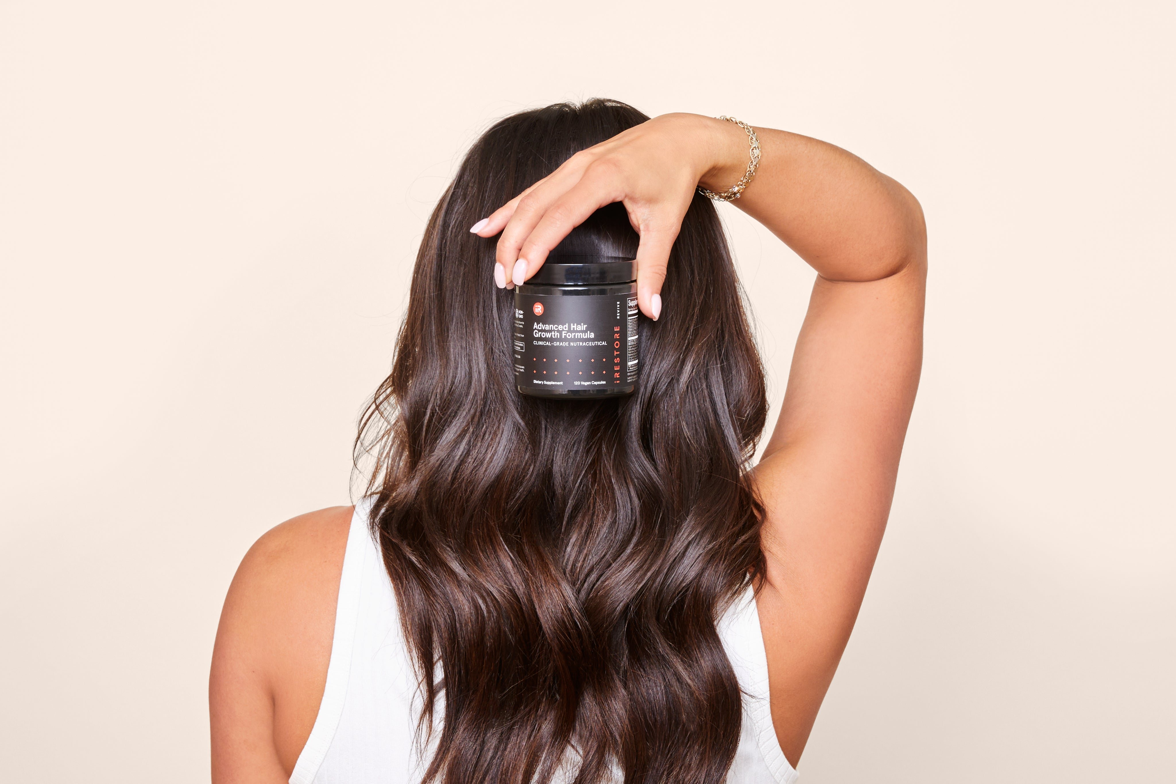 Woman with wavy hair holding a hair growth formula jar behind her back.