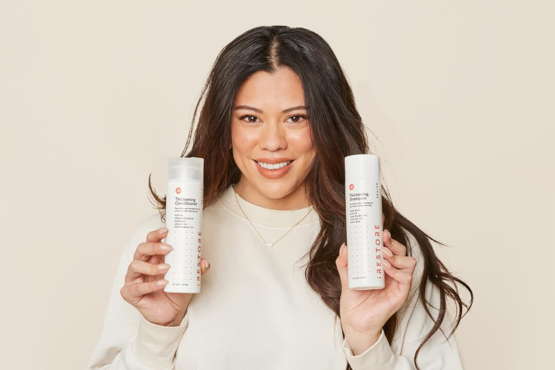 Image of a woman holding the Thickening Shampoo in her one hand and the Thickening Conditioner on her other hand.