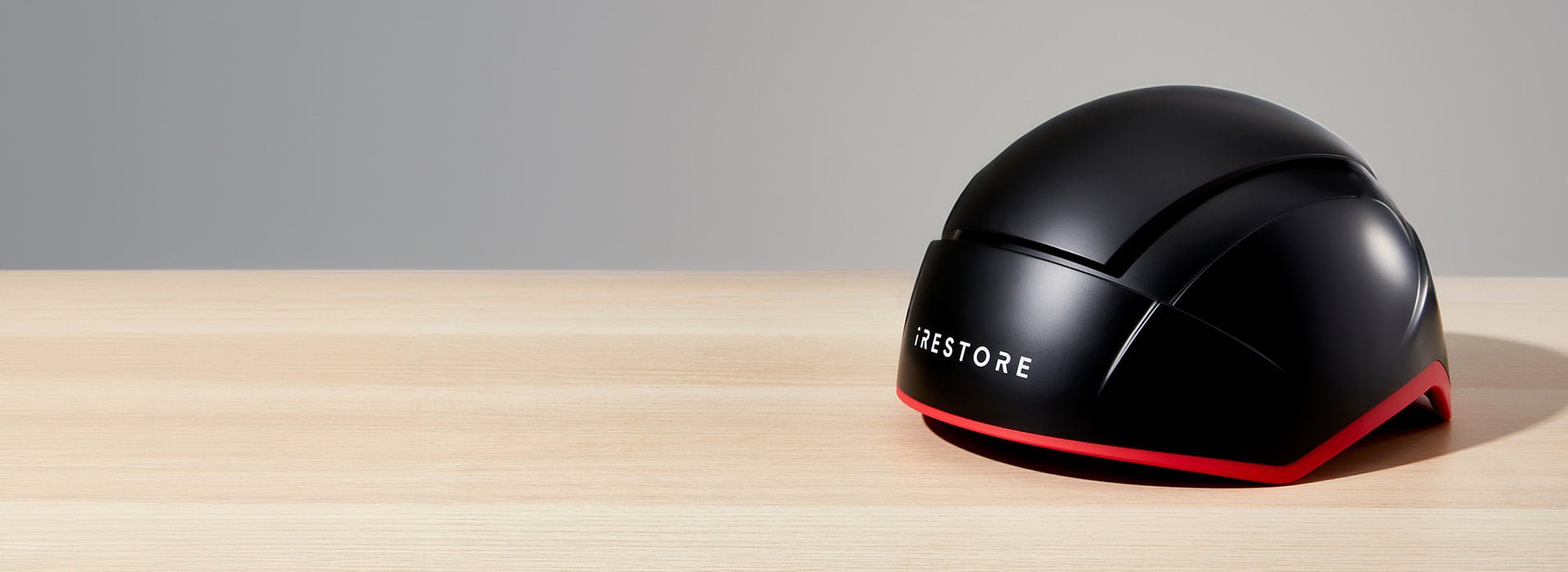 A black hair restoration helmet labeled 'iRestore' on a wooden surface against a neutral background.