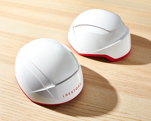 Two white iRestore hair growth helmets on a wooden surface.