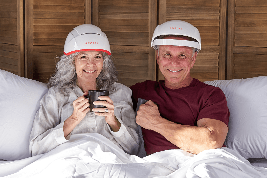 Image shows a mature man and woman relaxing on a bed while drinking in a mug. The man is wearing the Essential device while the woman is wearing the Professional device.