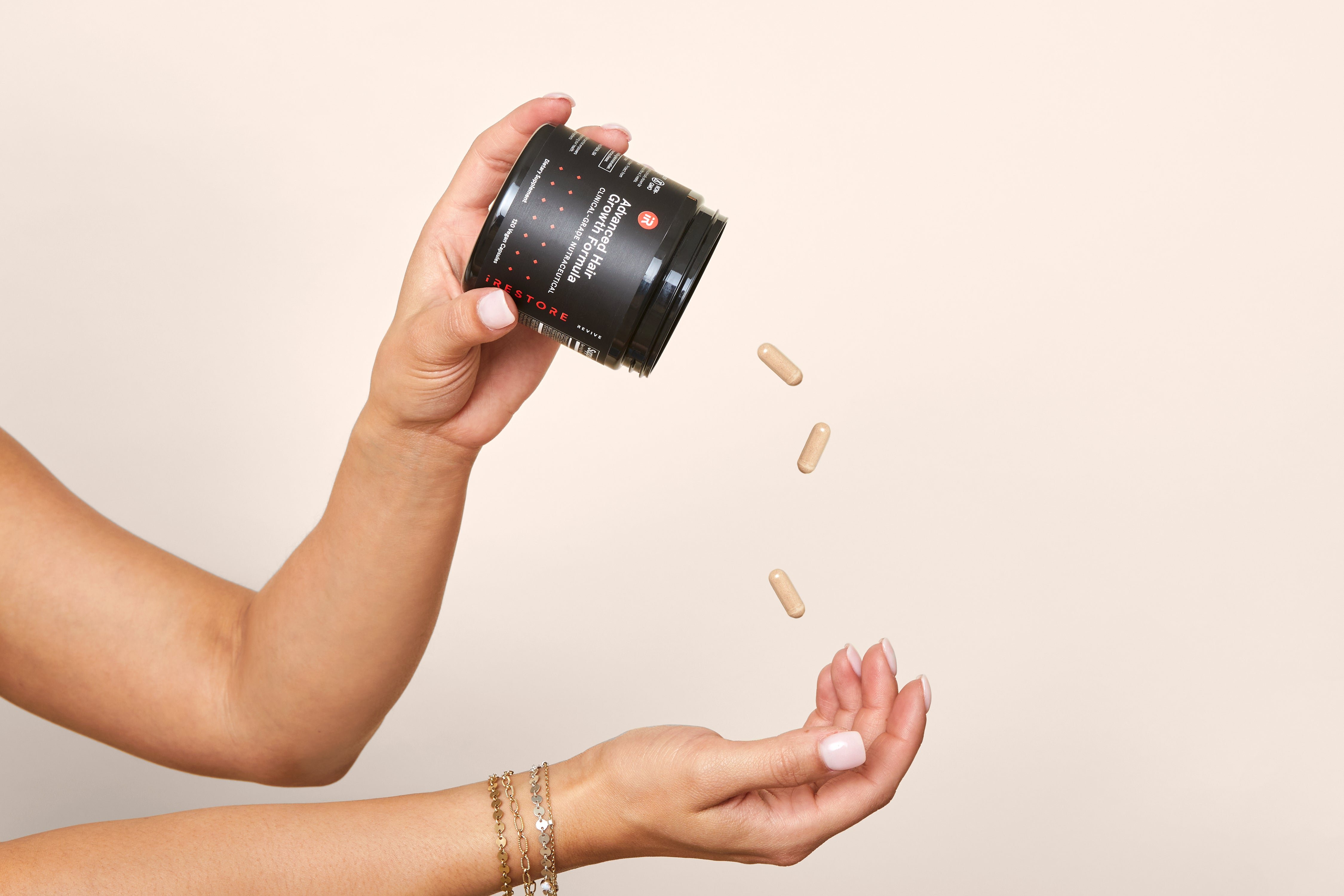 Hand catching capsules falling from a black supplement jar.