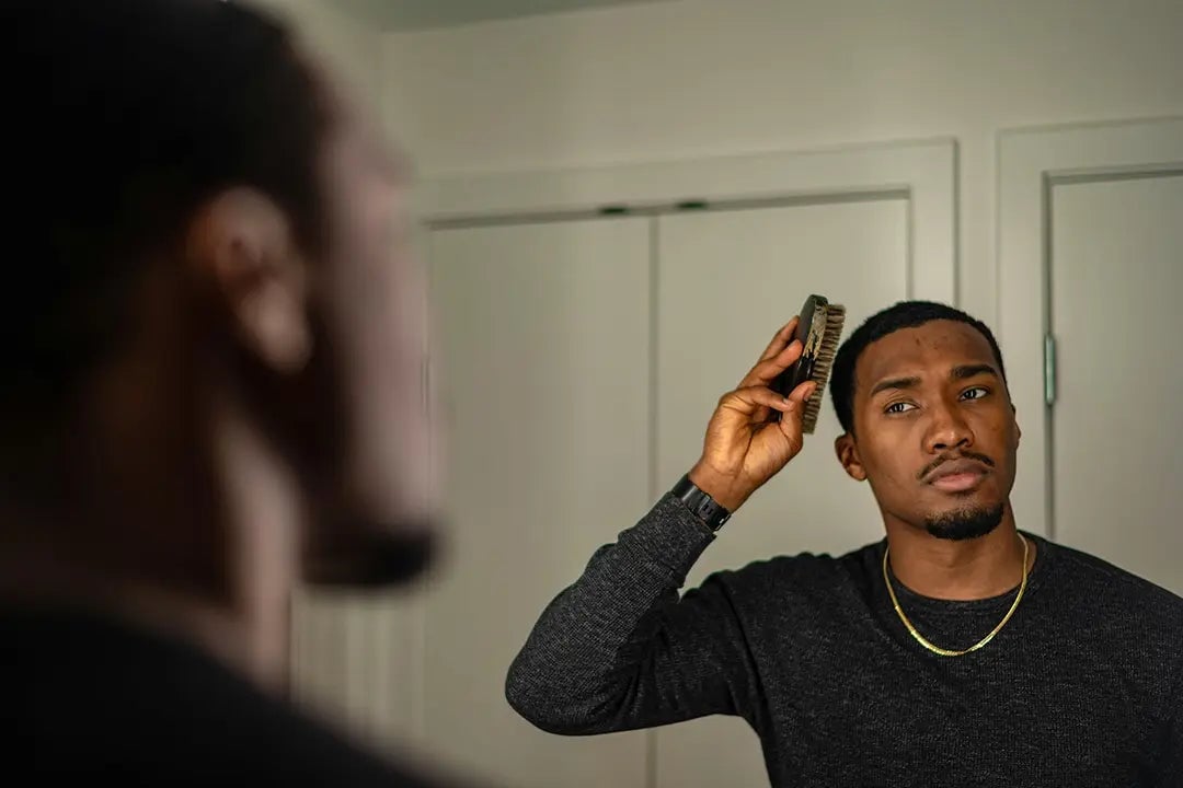 Man looking concerned at mirror with hairbrush in hand.